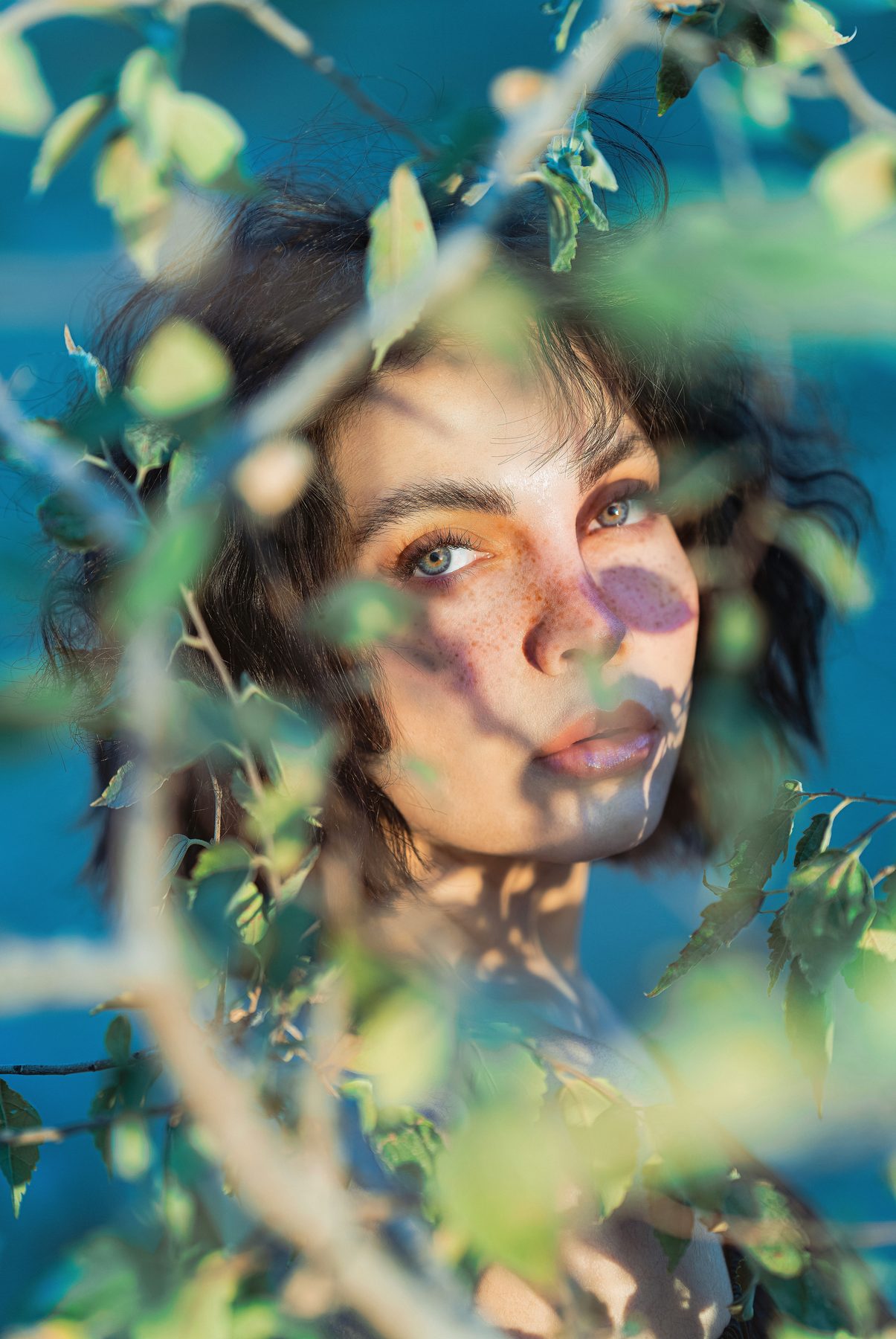 Portrait partly hidden by leaves in blue-green light